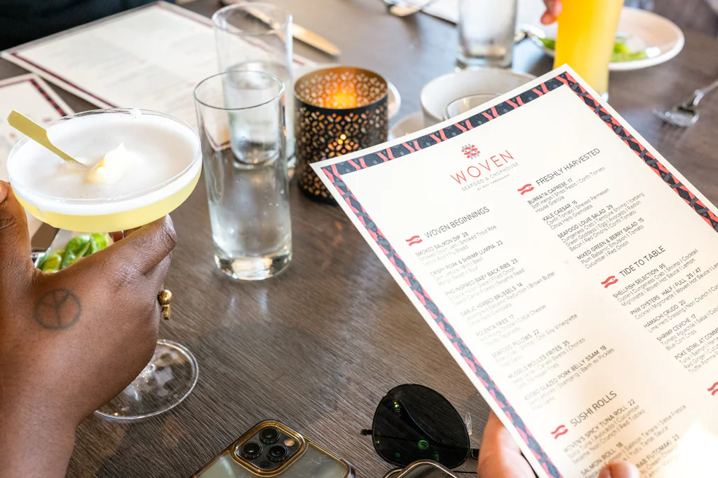 A person holding a cocktail next to a menu titled 