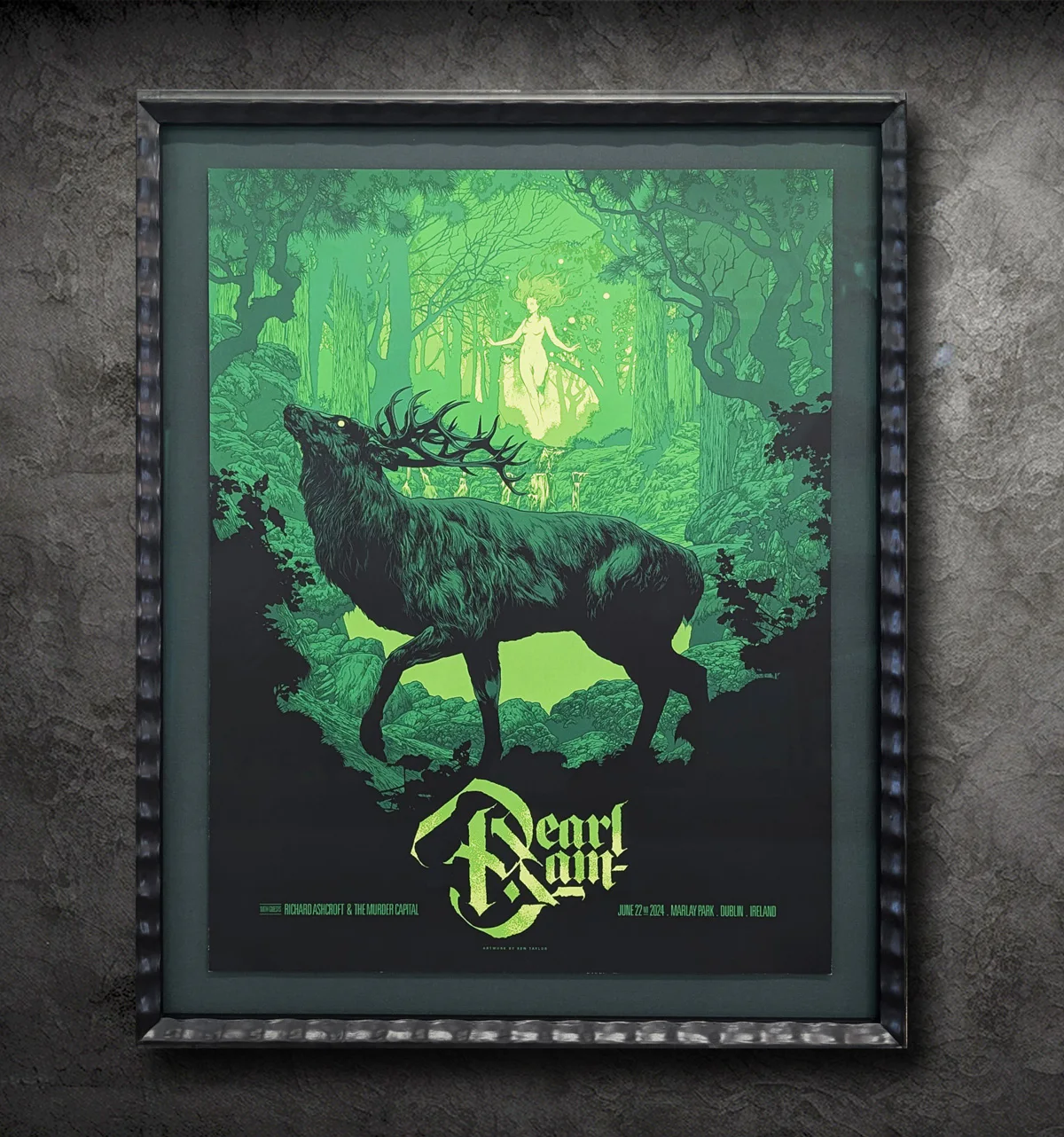 Framed poster of a concert with a large stag and a mystical figure in a forest. Text reads 
