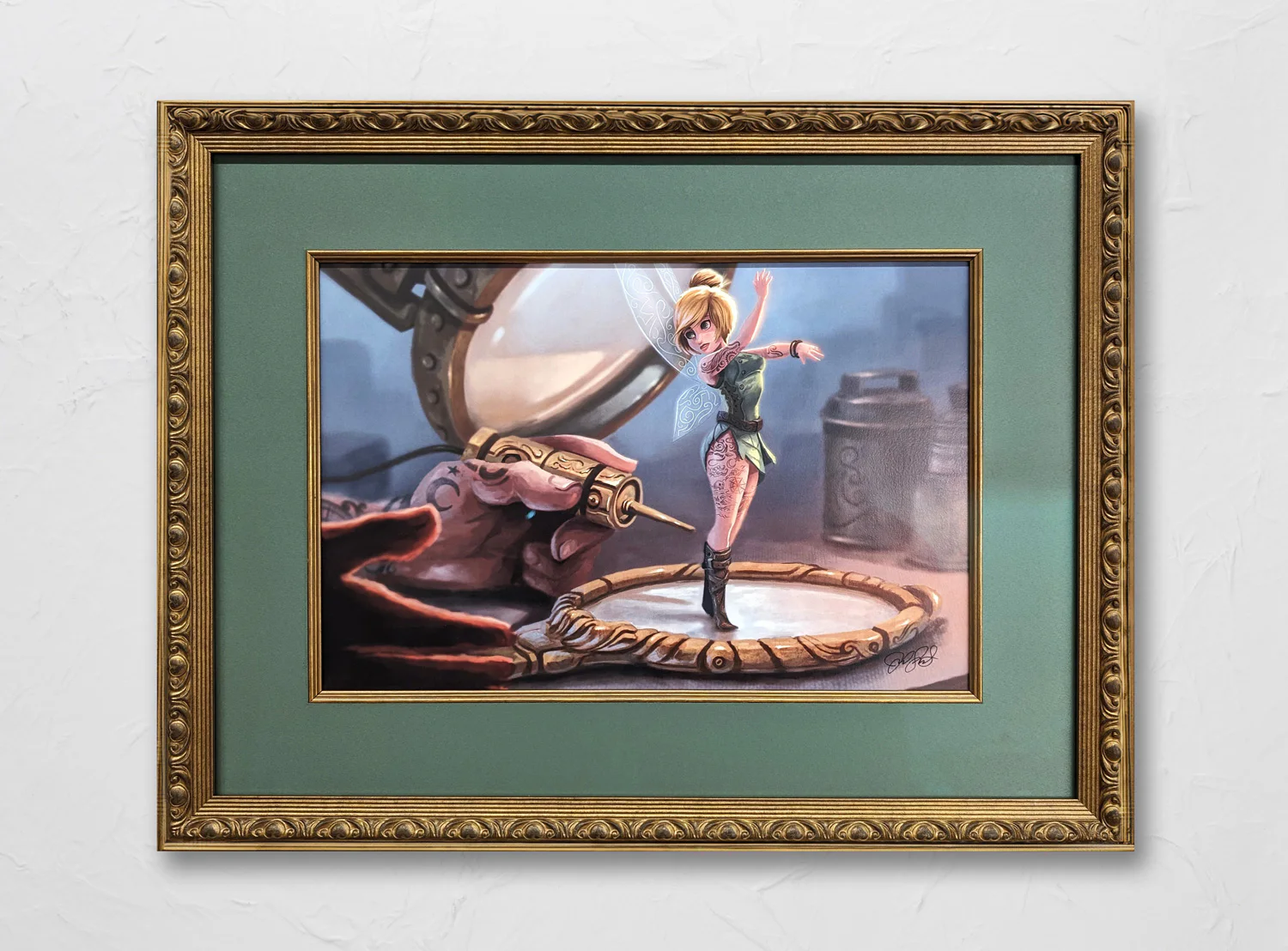 A framed artwork depicts a fairy in a green dress standing on a circular surface, raising her arms. A large hand holding a tattoo machine is drawing intricate designs on the fairy's body.