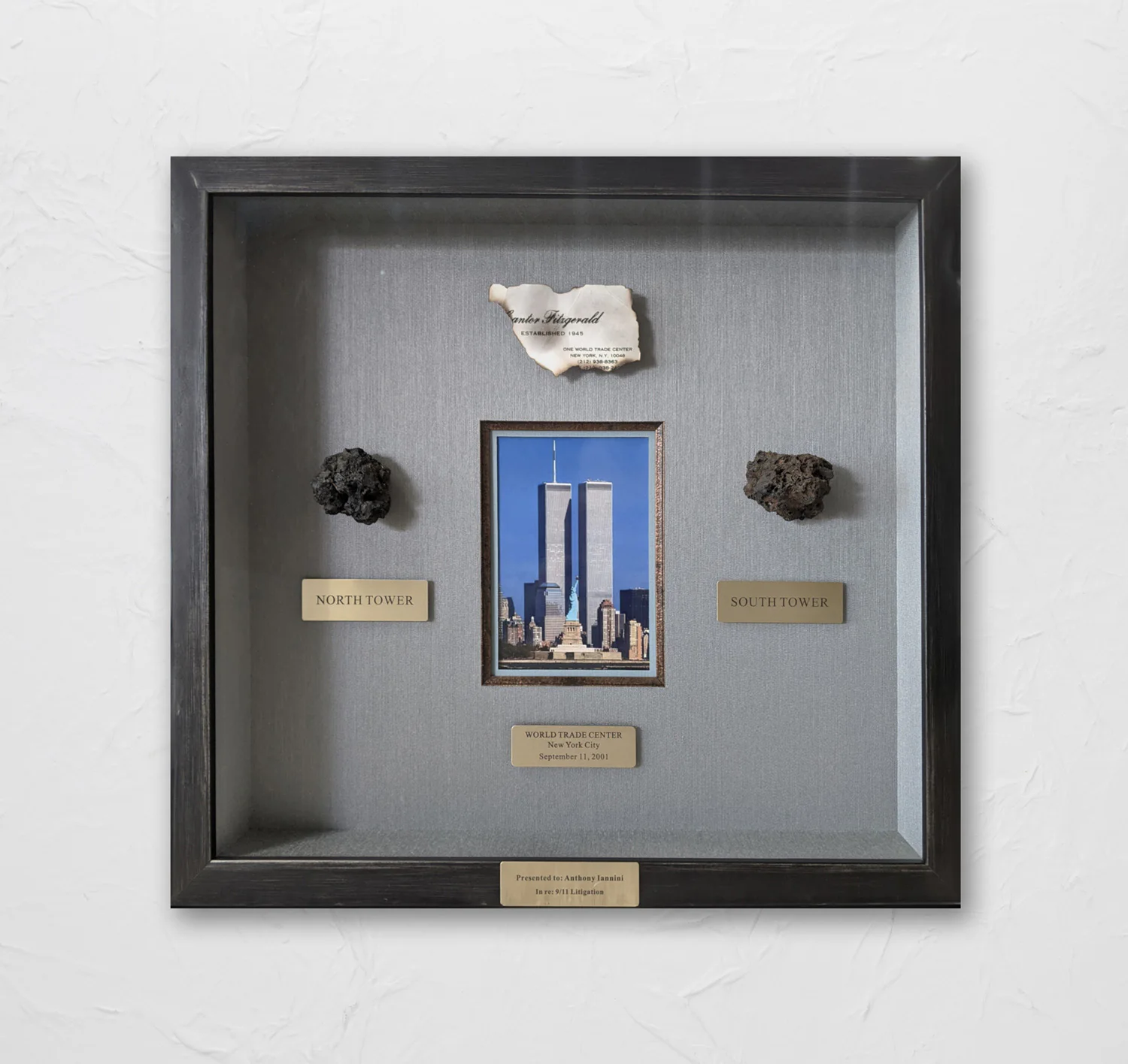 Framed memorabilia featuring a photo of the World Trade Center towers, labeled artifacts from the North and South Towers, and a burned document fragment. Plaque reads 