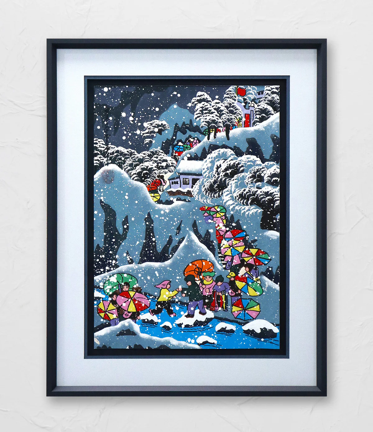 Framed painting of people holding colorful umbrellas on a snowy mountain path near houses, with snow-covered trees and mountains in the background.