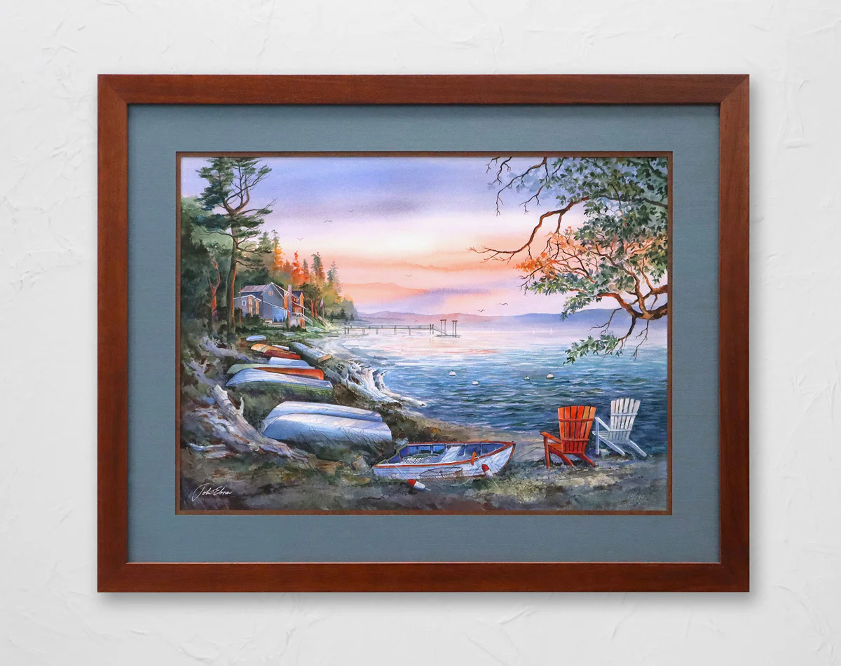 A framed painting of a lakeside scene at sunset, featuring small boats along the shore, houses among trees on the left, a dock in the distance, and two empty chairs by the water.