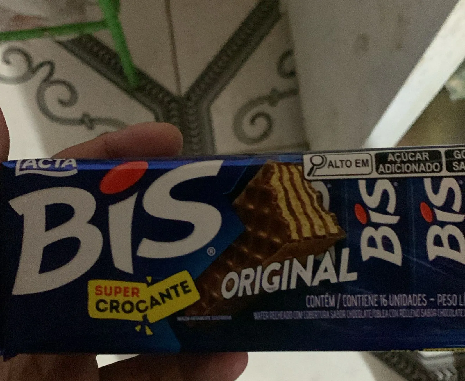 A hand holds a package of "BIS Super Crocante" chocolate wafers, labeled "Original." The blue packaging displays information in Portuguese and Spanish.